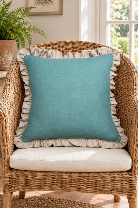 Square plain duck egg linen cushion with a gathered natural frill resting on a wicker chair.