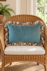 Plain duck egg rectangular cushion with a large natural linen frill on a wicker armchair.