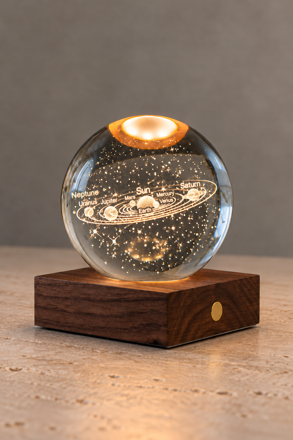 A clear glass or acrylic celestial globe lamp with etched solar system illustrations and stars, glowing from a warm light inside, displayed on a dark wood base against a neutral gray background.