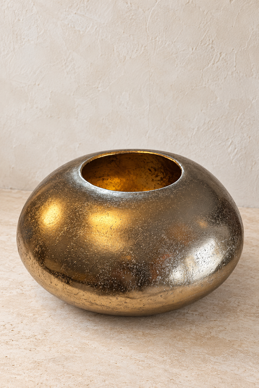 XL gold metal pebble bowl on a pale stone surface, showing its rounded body, mottled finish and narrow opening.