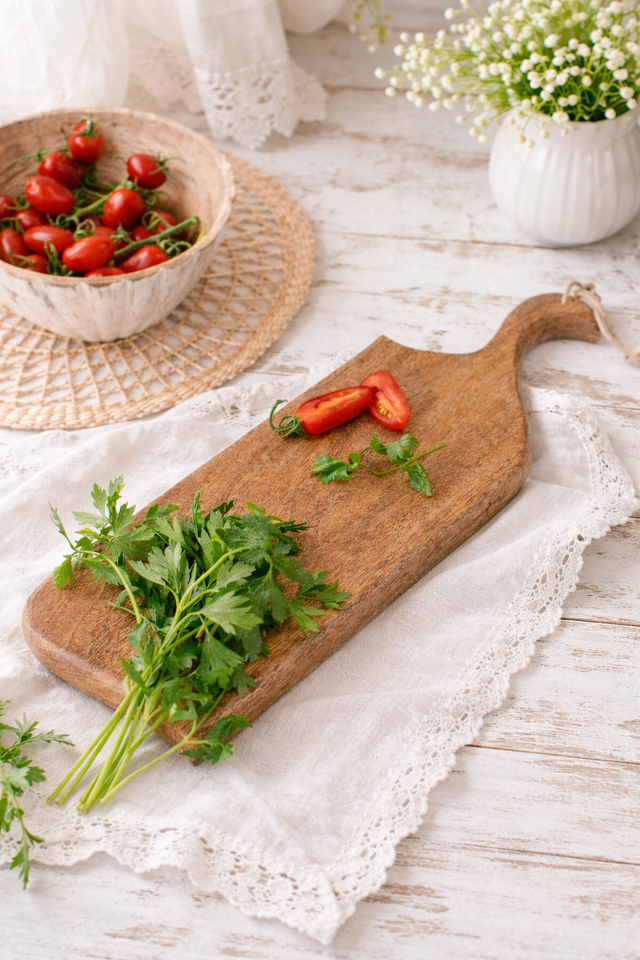 Wooden cutting board with fresh herbs and red peppers on a rustic wooden table.