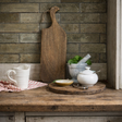 Wooden cutting board and kitchen items on a rustic wooden surface with a stone wall background.