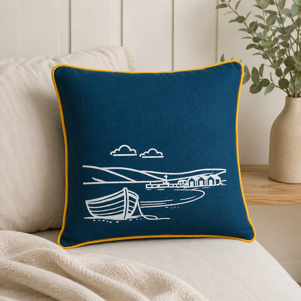 Fjære hand printed linen cushion cover in deep blue with white coastal boat design and mustard piping on a neutral sofa.