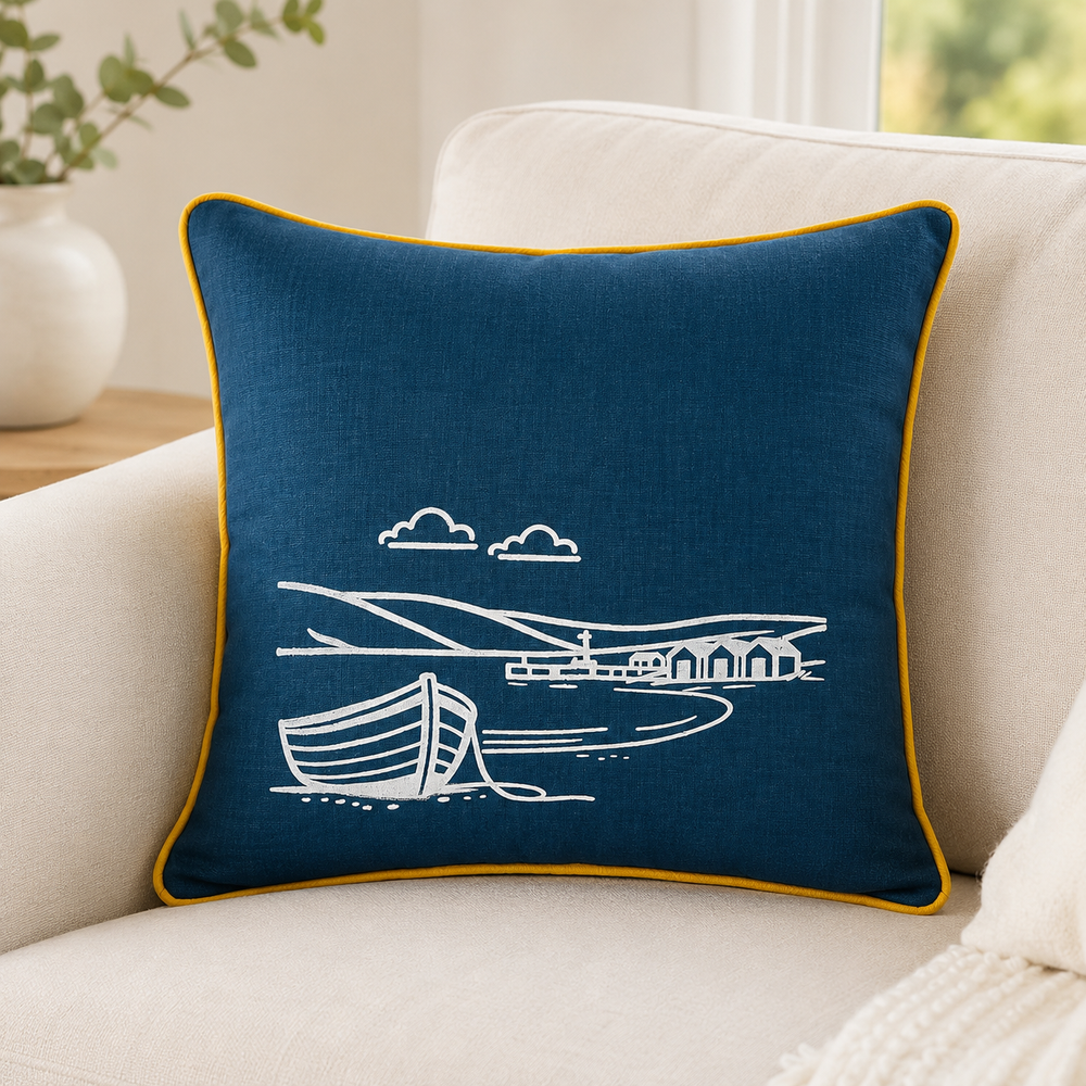 Fjære hand printed linen cushion cover in deep blue with white coastal boat design and mustard piping on a sofa.