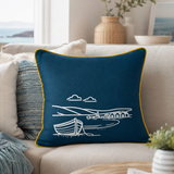 Fjære hand printed linen cushion cover in deep blue with white coastal boat design and mustard piping on a sofa in a beach house.