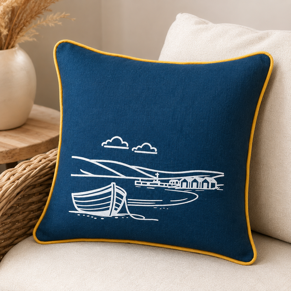 Fjære hand printed linen cushion cover in deep blue with white coastal boat design and mustard piping on a wicker sofa.