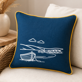 Fjære hand printed linen cushion cover in deep blue with white coastal boat design and mustard piping on a wicker sofa.