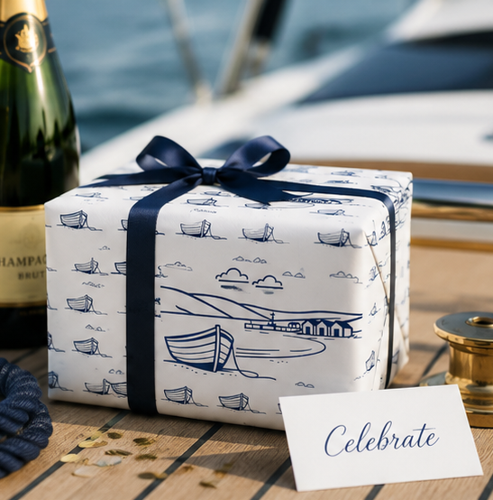 Gift wrapped in nautical-themed paper with a bottle of champagne on a boat.