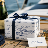 Gift wrapped in nautical-themed paper with a bottle of champagne on a boat.