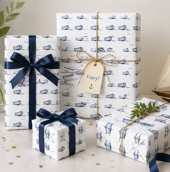 Three gift boxes wrapped in coastal theme wrapping paper with boat patterns, tied with Blue ribbons and a tag.