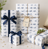 Three gift boxes wrapped in coastal theme wrapping paper with boat patterns, tied with Blue ribbons and a tag.