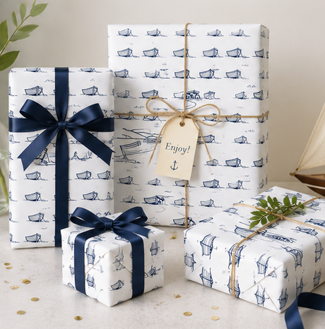 Three gift boxes wrapped in coastal theme wrapping paper with boat patterns, tied with Blue ribbons and a tag.