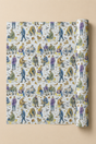 A roll of wrapping paper with a repeating watercolor-style pattern of people and dogs in autumn colors, shown partially unrolled against a solid beige background.