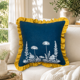Florilegium blue linen cushion cover with white botanical print and mustard ruffle edge styled on a sofa.