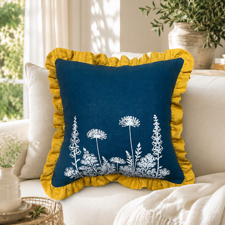 Florilegium blue linen cushion cover with white botanical print and mustard ruffle edge styled on a sofa.