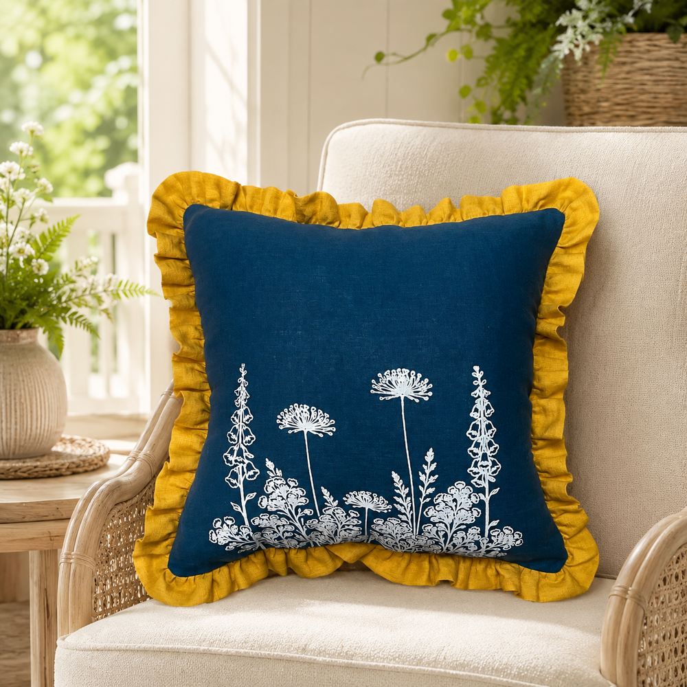 Florilegium blue linen cushion cover with white botanical print and mustard ruffle edge styled on a wicker chair.
