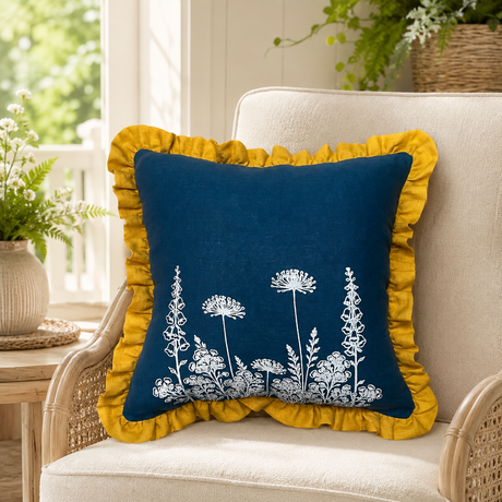 Florilegium blue linen cushion cover with white botanical print and mustard ruffle edge styled on a wicker chair.