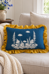 Rectangular blue Florilegium linen cushion with white botanical print and mustard ruffle on a pale sofa.