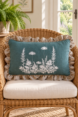 Rectangular duck egg cushion with white botanical print and natural linen frill on a wicker armchair.