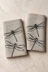 Two natural linen napkins with black dragonfly prints arranged on pale stone.