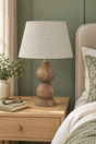 Frampton Medium brown mango wood table lamp with beige linen shade on a bedside table