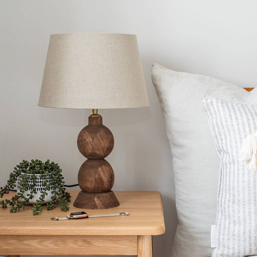 Frampton Medium brown mango wood table lamp with beige linen shade on a bedside table