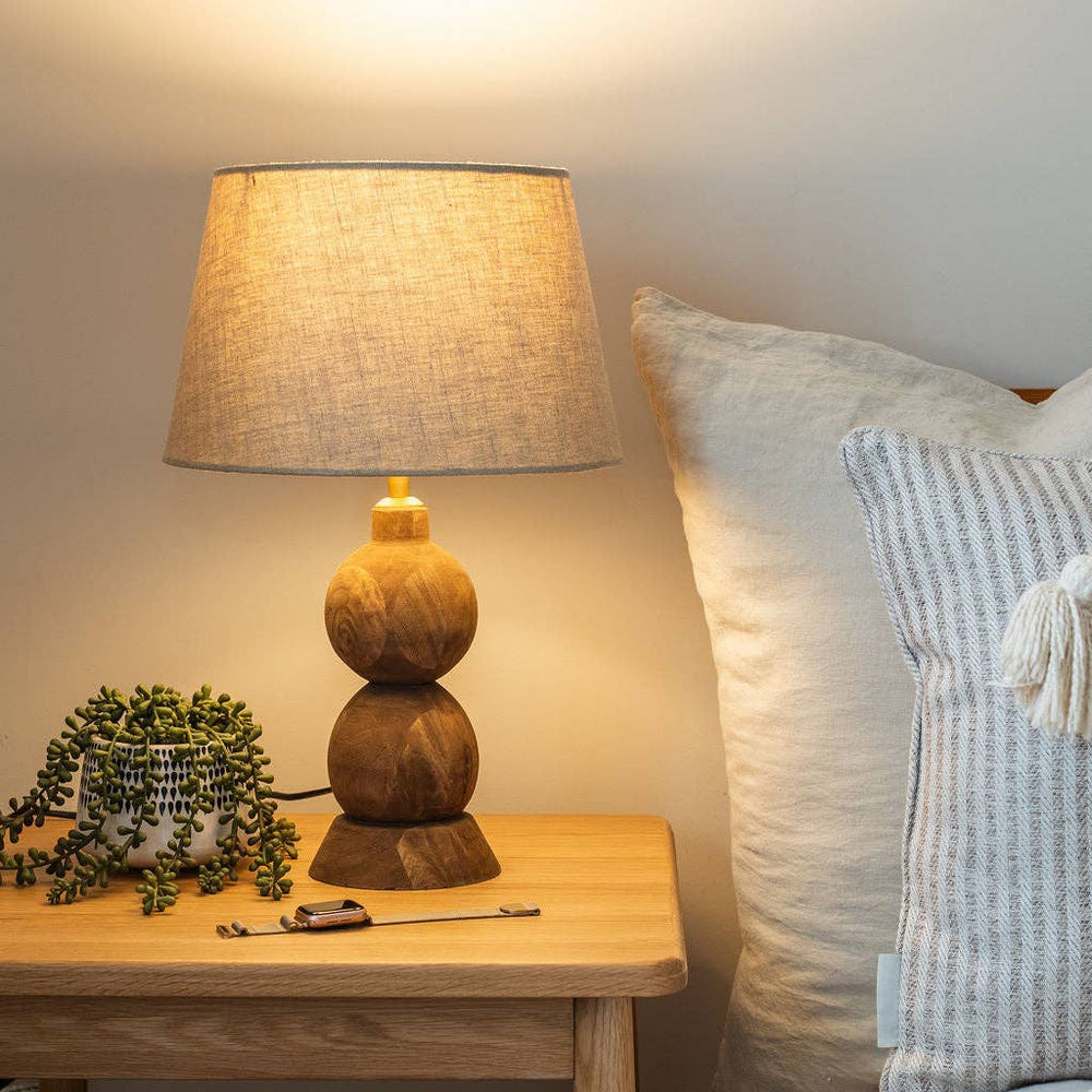 Frampton Medium brown mango wood table lamp with beige linen shade on a bedside table