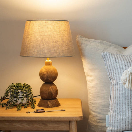 Frampton Medium brown mango wood table lamp with beige linen shade on a bedside table