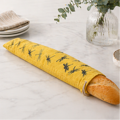 Yellow dragonfly patterned linen bread bag used to cover a French stick on a wooden board and table.