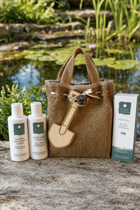 A mini hessian tote bag with a wooden shovel charm sits on a stone surface outdoors with Pure Lake products Foot Gel, Anti-insect lotion and after sun lotion.