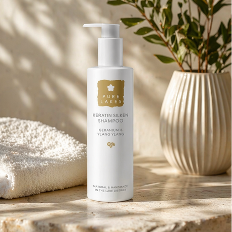 White shampoo bottle with pump labeled 'Pure Lakes' on a wooden surface with a towel and plant in the background.