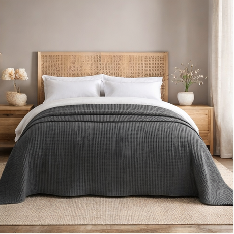 Grey quilt draped over a bed in bedroom setting.