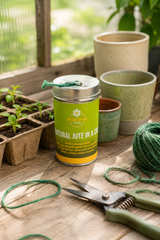 Green container labeled 'Natural Jute in a Can' on a wooden surface with gardening tools and plants.