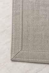 Close-up of a natural linen dragonfly napkin showing its mitred corner, double-fold hem and pale stitching.