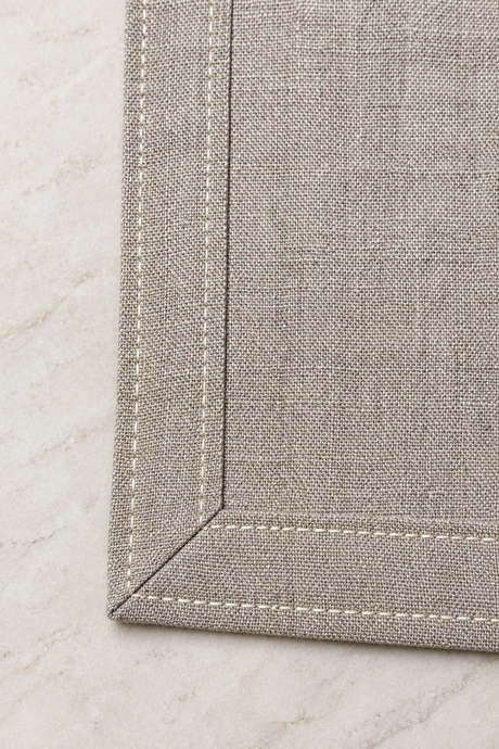 Close-up of a natural linen dragonfly napkin showing its mitred corner, double-fold hem and pale stitching.