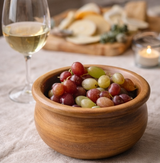Wooden bowl of grapes with a glass of white wine on a table.