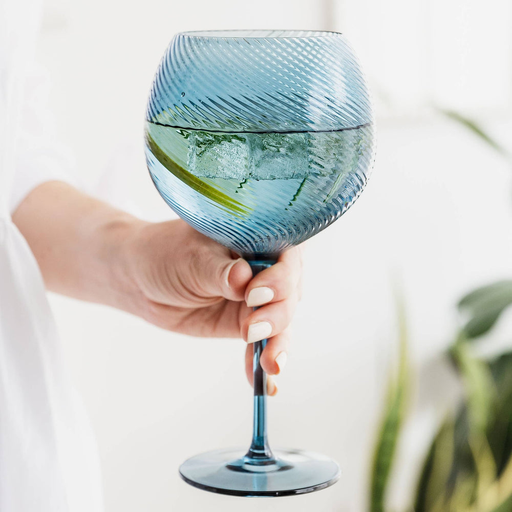 Hand holding a blue twist design glass with a plant in the background