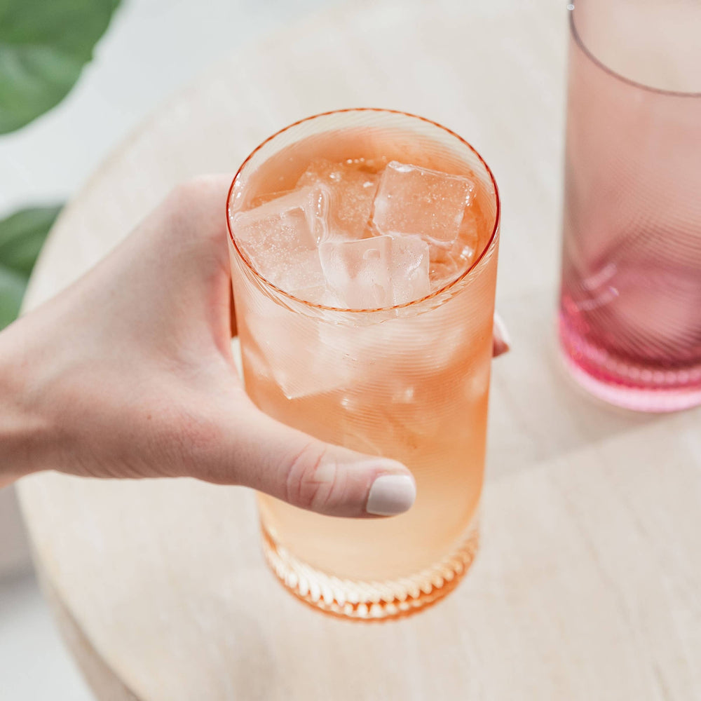 Hand holding a glass of pink iced drink with a blurred background