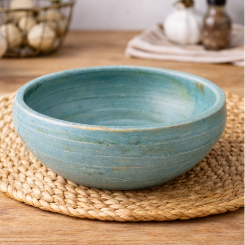 Handcrafted ceramic bowl on a wooden surface with herbs and oil.