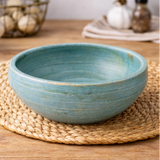 Handcrafted ceramic bowl on a wooden surface with herbs and oil.