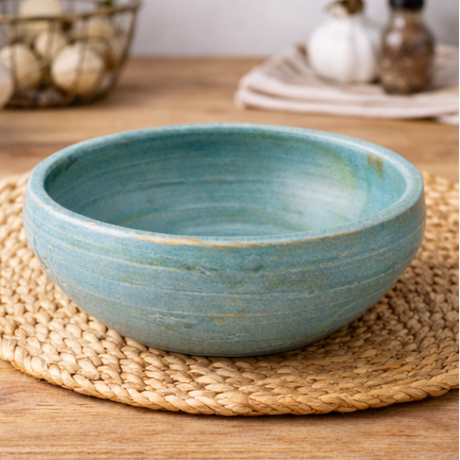 Handcrafted ceramic bowl on a wooden surface with herbs and oil.