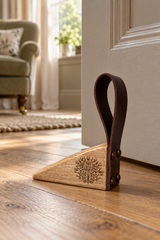 A wooden and leather door stopper resting on a hardwood floor in front of a white door, with a softly blurred living room in the background.