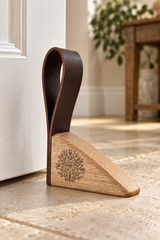 A wooden and leather door stopper placed on a stone floor next to a white door, with a blurred interior room in the background.