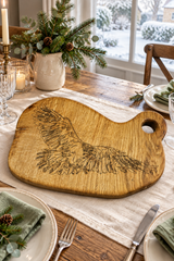 A rustic wooden serving board shaped like a painter's palette, engraved with a detailed eagle design, displayed on a decorated holiday dining table.