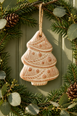 A handcrafted terracotta Christmas tree ornament in a warm terracotta pink colour, hanging from a natural jute string. The ornament features embossed patterns of stripes, circles, and dots.