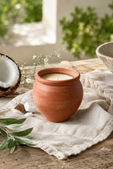 Terracotta pot with a coconut scented candle on a wooden surface with plants in the background