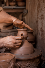 Person shaping a clay pot on a pottery wheel in a workshop.