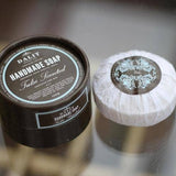 Handmade soap in a black container and white bar on a reflective surface