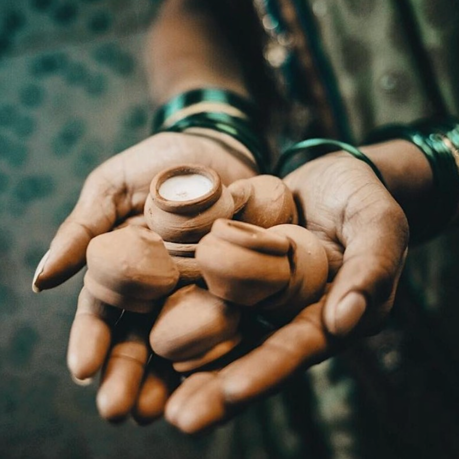 Hands holding a small hand made candles in clay pots with green patterned fabric background