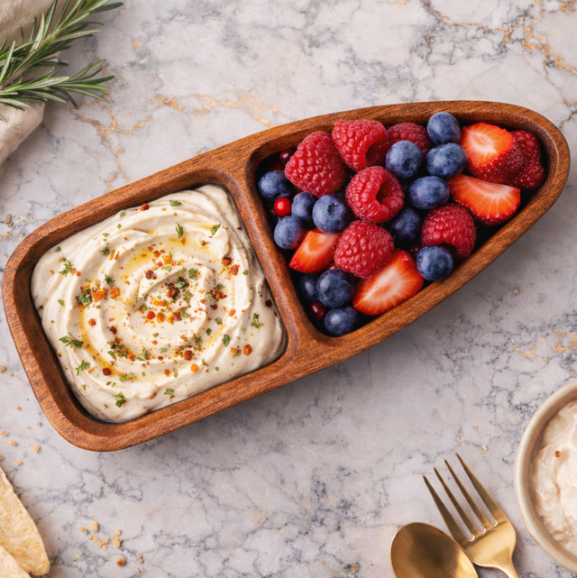 Wooden boat-shaped serving tray with dip and berries on a marble surface